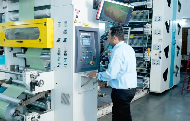 Man operating a control panel on industrial printing machinery in a factory.