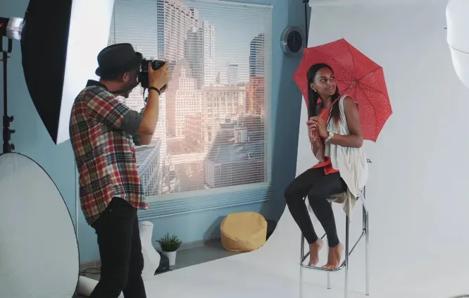Photographer capturing a woman posing with a red umbrella in a professional studio setup.